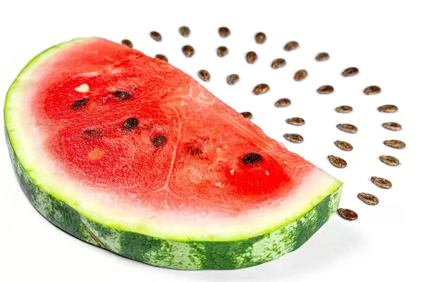 Slice of fresh watermelon and its seeds on white background