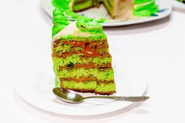Slice of homemade green cake on a platter with a spoon