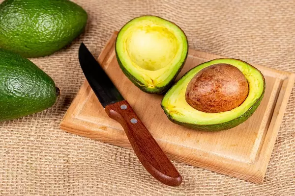 Sliced avocado with knife on wooden kitchen board with burlap