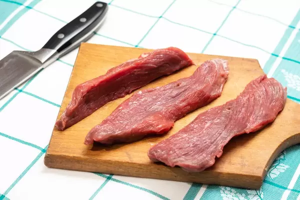 Sliced beef meat on the kitchen board with knife in the background