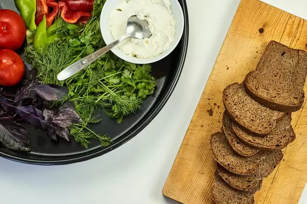 Sliced bread, and a bowl of organic raw bell peppers, tomatoes. parsley and sour cream