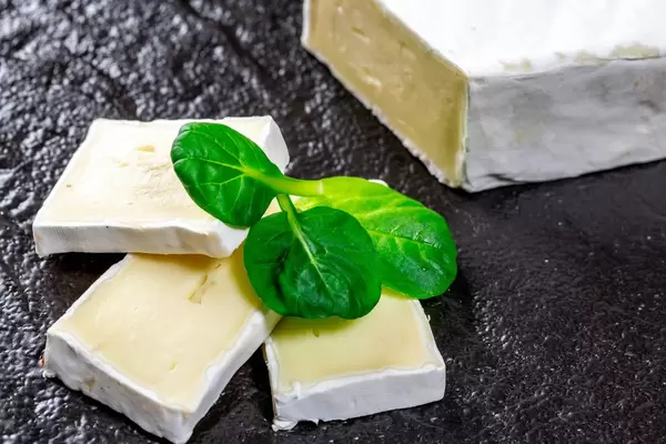 Sliced brie cheese with greens on black background