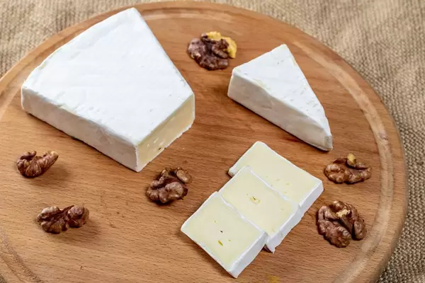 Sliced brie cheese with walnut kernels on a round kitchen Board