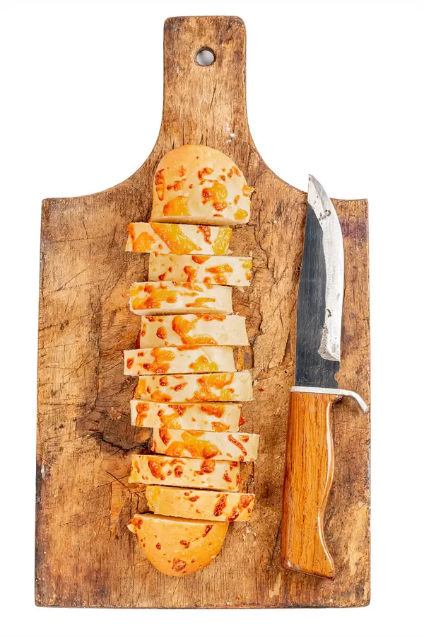 Sliced cheese baguette pieces on an old wooden board with a knife, top view