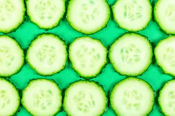 Sliced cucumber slices on a green background, top view (Flip 2020)