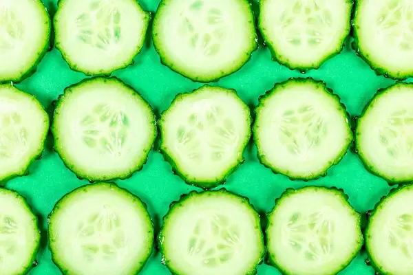 Sliced cucumber slices on a green background, top view