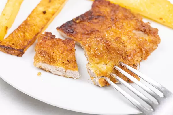 Sliced fried pork meat on the fork with fried potatoes on the plate