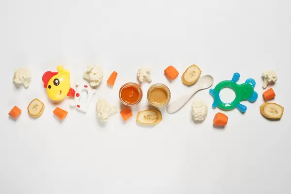 Sliced fruits, vegetables, baby food puree bottles and toys on white background