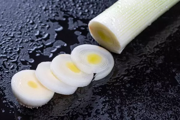 Sliced leek rings on black background with water drops