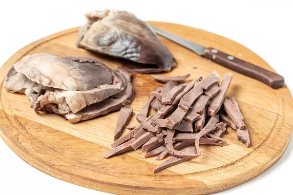 Sliced pieces cooked heart on a wooden kitchen board with a knife
