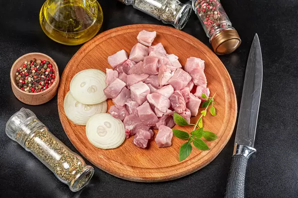 Sliced raw pork meat with spices and a knife on a dark background
