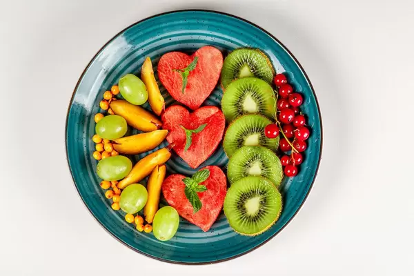 Sliced ripe fresh fruit and berries in a plate on a white background, top view