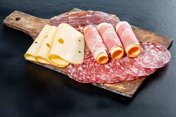 Sliced salami, ham, and cheese on an old kitchen wooden Board on a black background (Flip 2019)