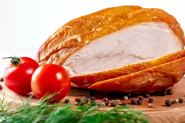 Sliced smoked chicken breast with herbs and spices on wooden cutting board