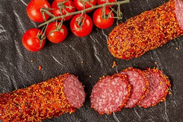Sliced smoked sausage with spices and tomatoes on a dark background