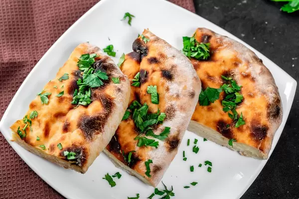 Sliced traditional cheese khachapuri on a plate with greens