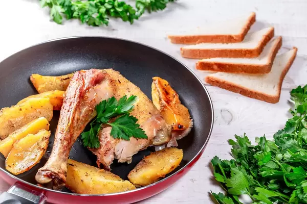 Slices of fried potatoes with chicken in a frying pan