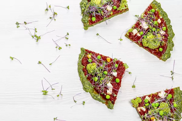 Slices of vegetarian vegetable pizza with micro-green cabbage on a white wooden background. Top view
