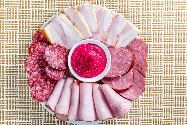 Slicing of ham and different varieties of sausage on a plate with sauce