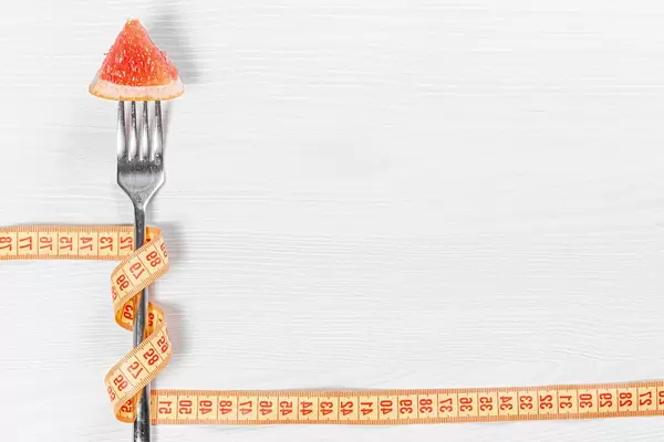Slimming concept-a piece of grapefruit on a fork wrapped with measuring tape on a white wooden background (Flip 2019)