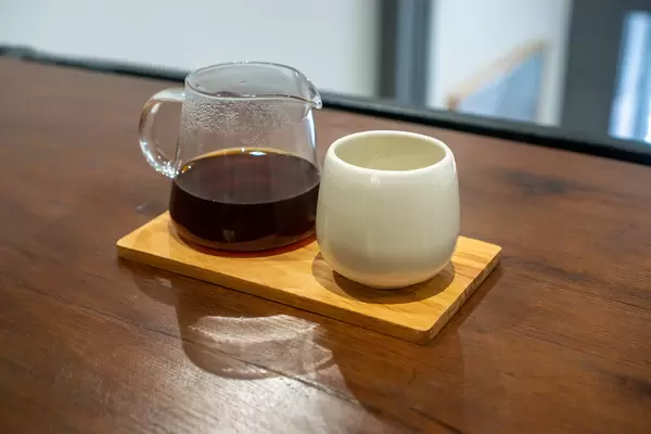 Small Glass Jug with Hot Dripping Coffee on a Wooden Serving Board with a White Ceramic Cup