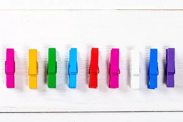 Small, multicolored cloth hangers on the white wooden background