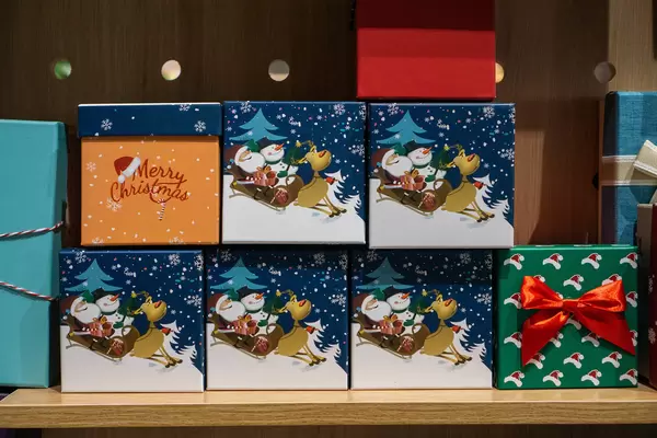 Small Paper Present Box in Christmas Design with Santa Claus, Snowman and Raindeer displayed in a Store Shelf