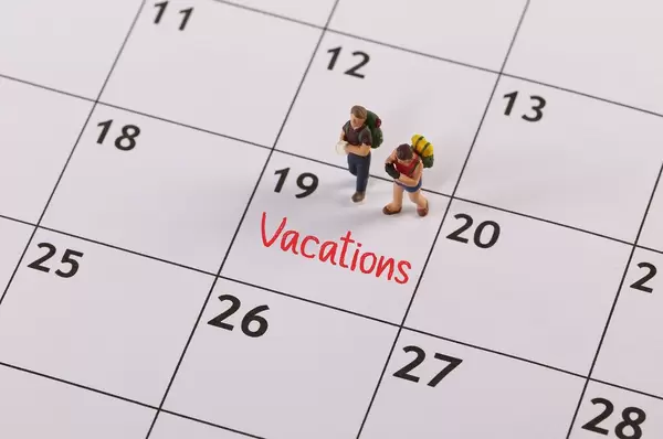Small traveler figures with backpack standing on calendar with Vacations text