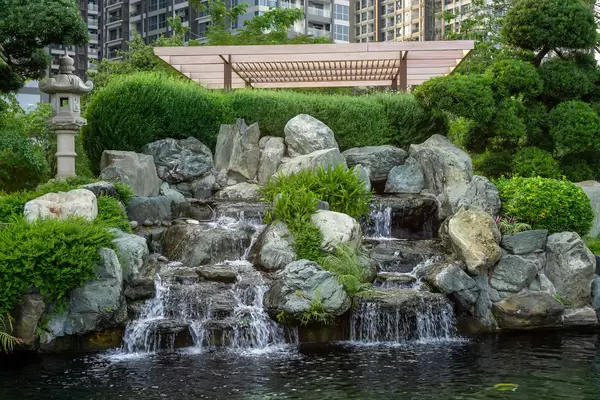 Small Waterfall with Rocks and Flowers into a Fish Pond with Koi Fish at Vinhomes Central Park in Ho Chi Minh City, Vietnam