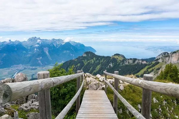 Small wooden bridge on the hiking trail in Swiss Alps with the view of mountains and lake Geneva