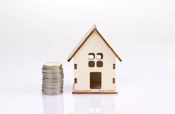Small wooden house with coin stack on white background