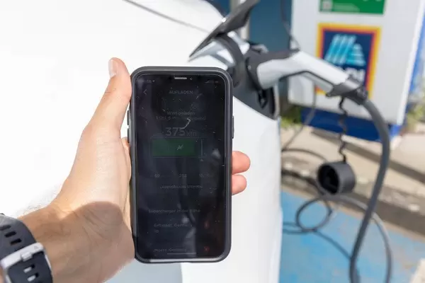 Smartphone app displays the charging bar in kilometre, while the Tesla electric car is charged with solar energy on an Aldi car park in Germany
