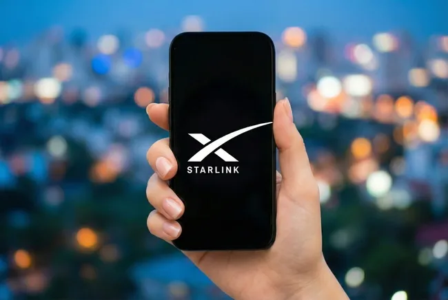 Smartphone mit Starlink-Logo vor Stadtlichtern