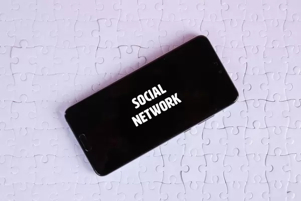 Smartphone on a white jigsaw puzzle with Social Network text