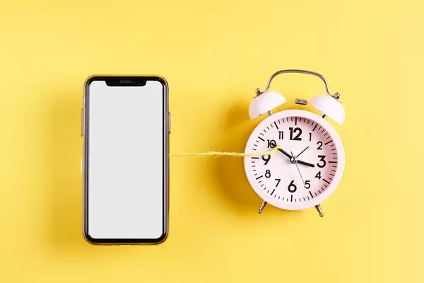 Smartphone with blank screen and classic alarm clock tied with a rope