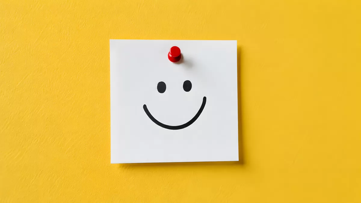 Smiley auf weißem Notizzettel an gelber Wand