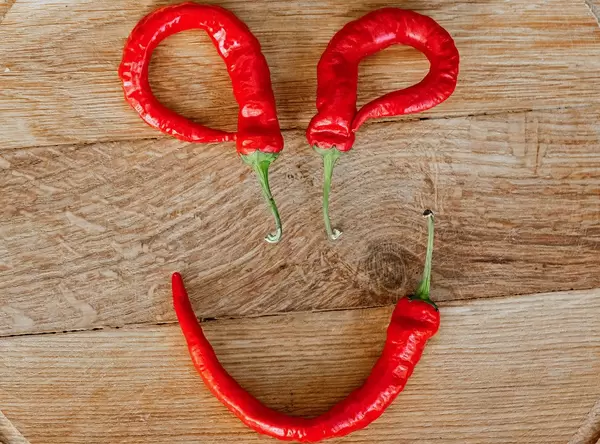 Smiley made of chili peppers on wooden background, top view