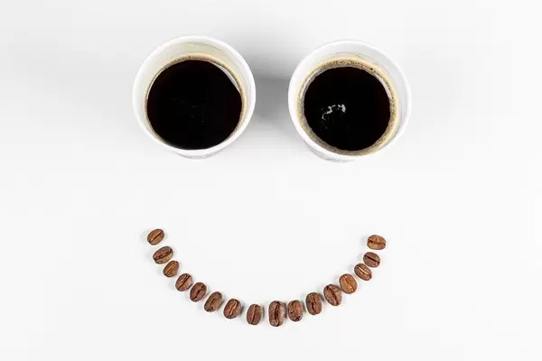 Smiling face - with coffee beans mouth and eyes from two paper cups of coffee. The concept of a good mood, a good start to the day