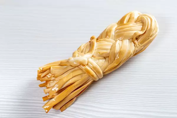 Smoked cheese Suluguni pigtail on white wooden background (Flip 2019)