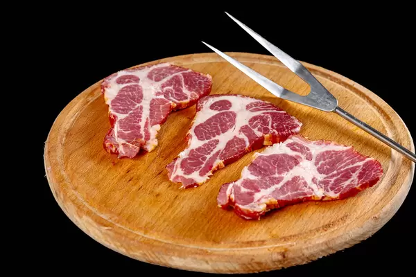 Smoked cured meats on wooden round kitchen board with fork