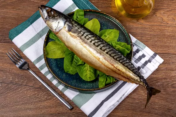 Smoked mackerel with spinach leaves in a plate on a wooden background