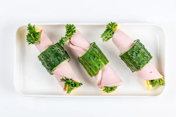 Snack rolls with vegetables, sausage and cheese on a white plate, top view