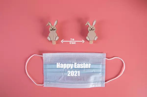 Social distancing concept with cute Easter bunnies, medical face mask and Happy Easter 2021 text
