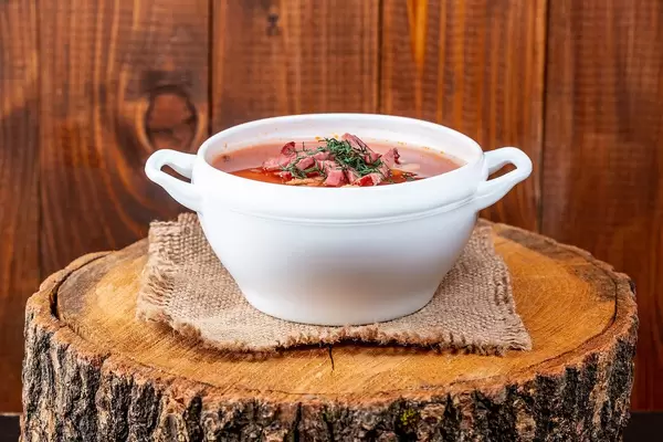 Soljanka- Suppe, aus der osteuropäischen Küche, in einer weißen Terrine und auf einem Baumstumpf serviert