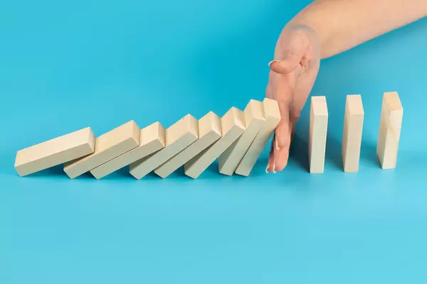 Solution concept with hand stopping wooden blocks from falling in the line of domino