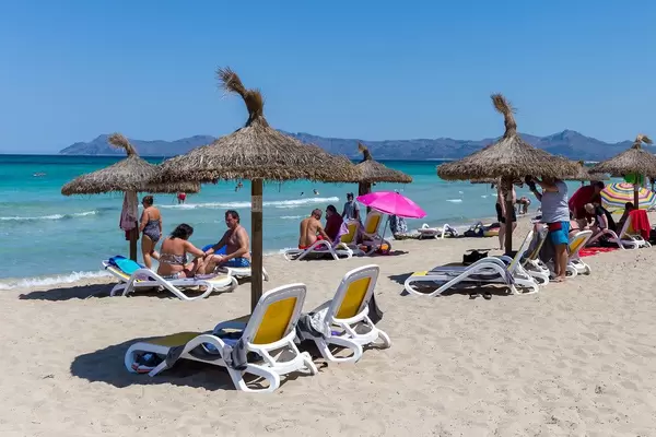 Sonnenschirme aus Stroh und Sonnenliegen. Touristen am Strand auf Mallorca im Sommer 2020