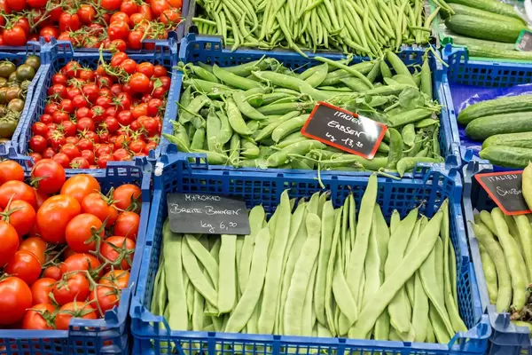 Sortierte Gemüseauslage mit Tomaten, Bohnen, Erbsen und Gurken in blauen Kunststoffboxen