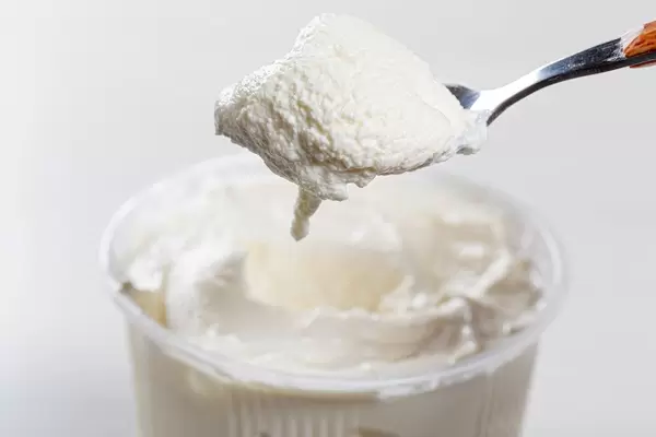 Sour cream in spoon and in plastic packaging