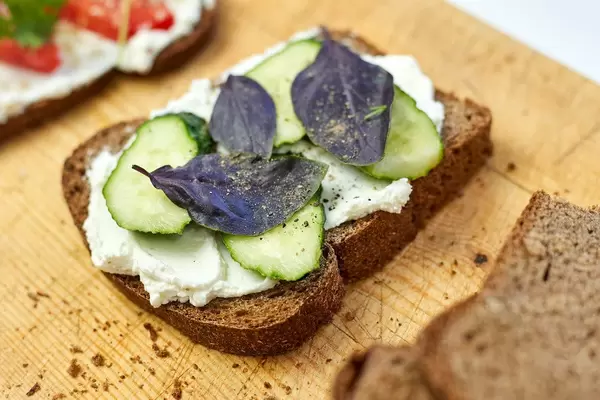 Sour cream spread on toast with cucumber slices and basil leaves
