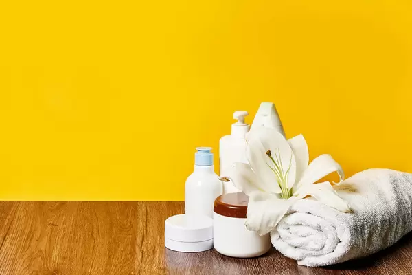 Spa beauty background with tools and cosmetics: creams, oils and towels on against yellow background